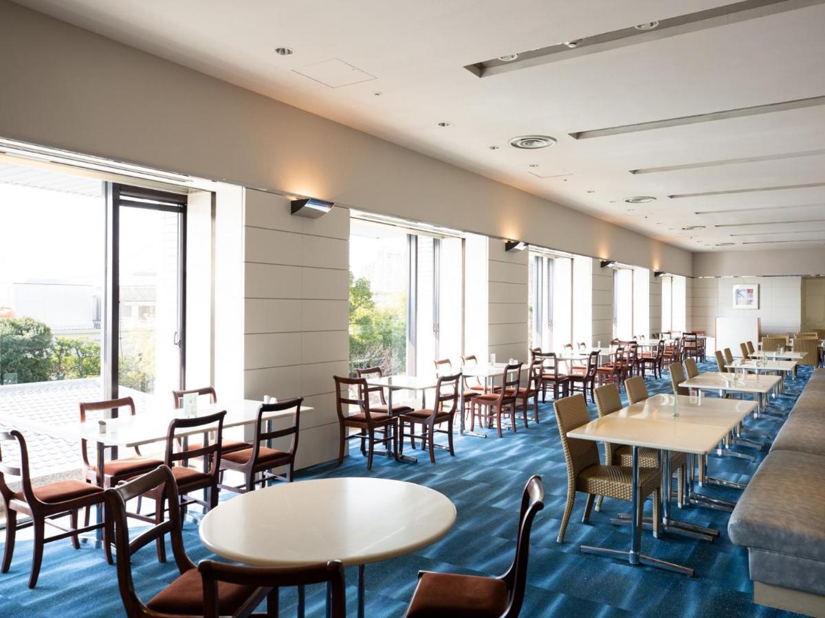 Hotel Okura Kōbe Exterior foto The photo depicts an interior space, likely a dining area or a café. It features several tables and chairs arranged throughout the room. The flooring is blue, and large windows line one side, allowing natural light to fill the space and providing a v