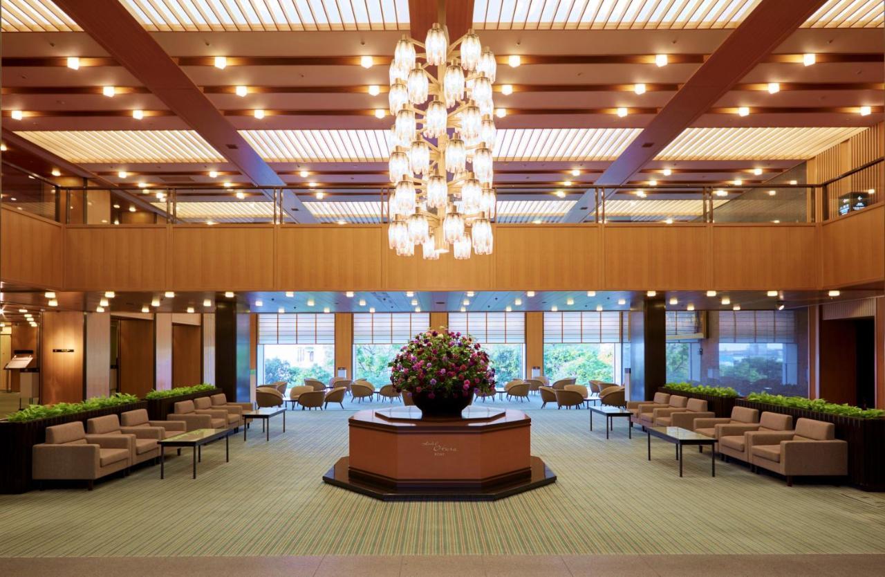 Hotel Okura Kōbe Exterior foto The photo shows a spacious, elegantly designed lobby. It features a large chandelier hanging from the ceiling, illuminating the space with soft light. There is a round reception desk or information counter in the center, adorned with a bouquet of col