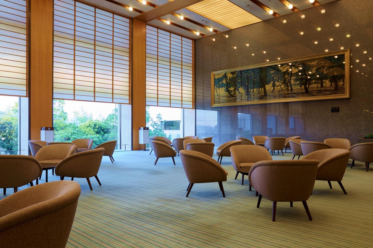 Hotel Okura Kōbe Exterior foto The photo shows a spacious, modern lounge area with a minimalist design. There are several comfortable, curved armchairs arranged throughout the space, all facing inward. The room features large windows with wooden blinds that allow natural light to 