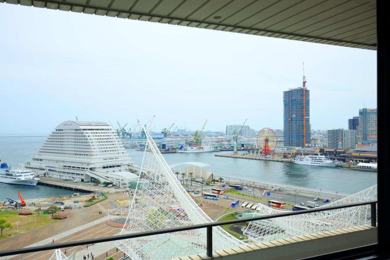 Hotel Okura Kōbe Exterior foto The photo shows a coastal urban landscape, likely of a port or waterfront area. In the foreground, there are modern structures, including a distinctive building with a curved roof, suggesting it could be a museum or exhibition center. The area is lin
